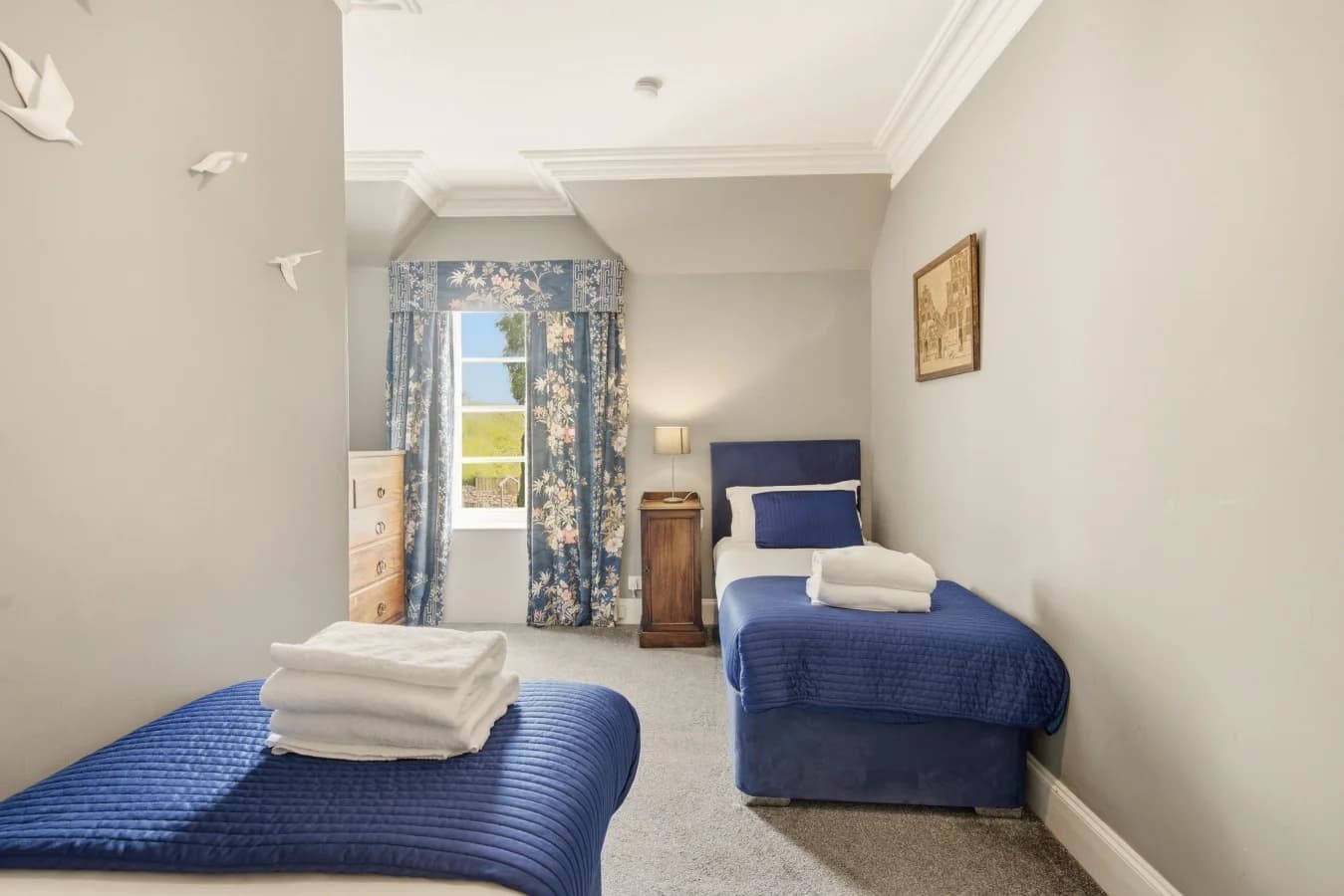 Twin bedroom with blue beds, grey walls and patterned curtains