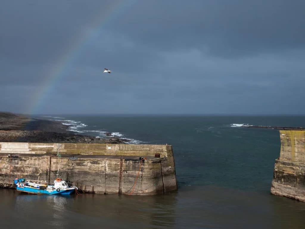 Dramatic coastal view across Craster Harbour, complete with a rainbow over the North Sea.