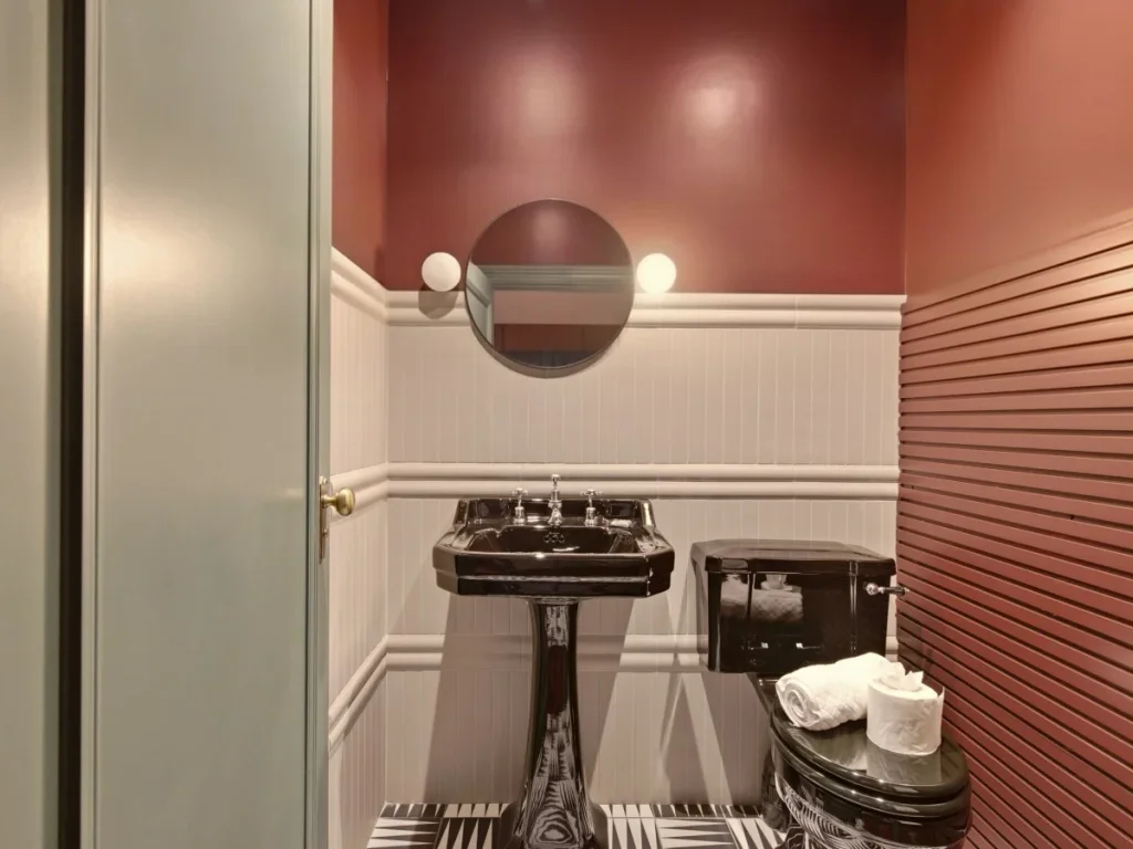 Black pedestal basin and WC with round mirror and feature wall lighting.