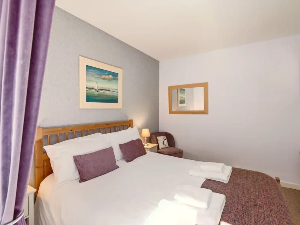 King bedroom with wooden bed frame, bedside lamps and purple accents