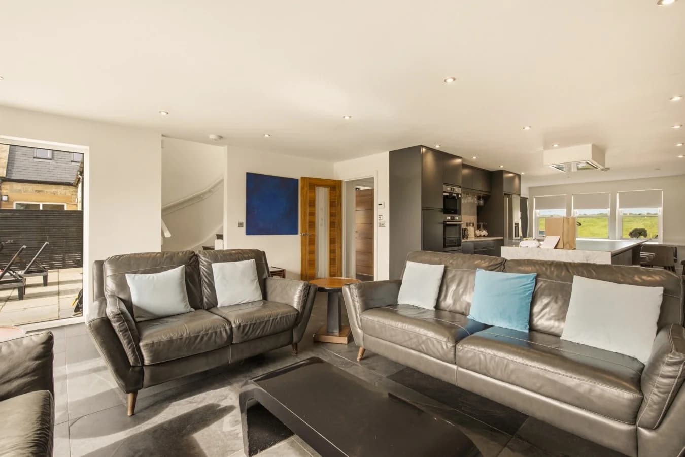 Open-plan lounge with leather sofas and modern kitchen beyond
