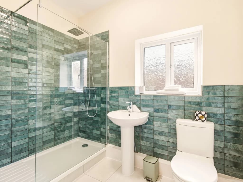 Bathroom with walk-in shower, blue tiled walls and frosted window.