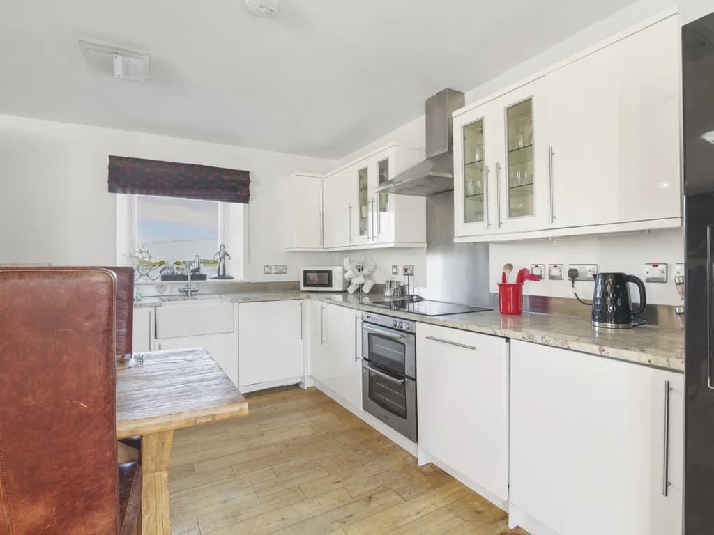 Bright, cozy kitchen with white cabinetry and timber flooring.