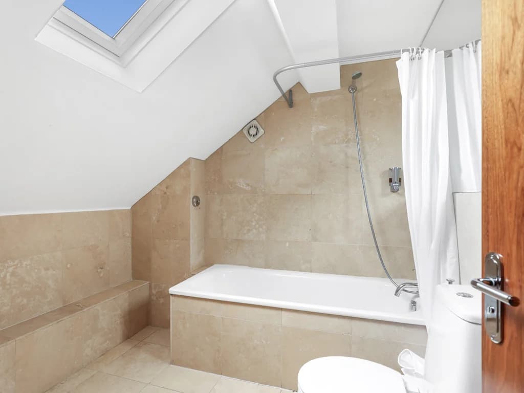 Family bathroom with bath, skylight and beige stone-effect tiling