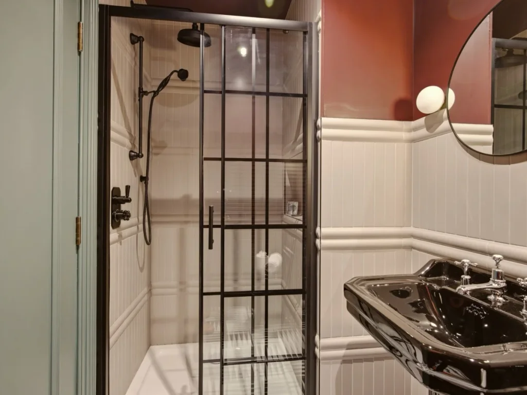 Modern shower room with walk-in shower, black basin and round mirror.