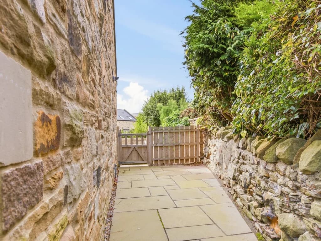 Gated side pathway bordered by stone walls and mature greenery