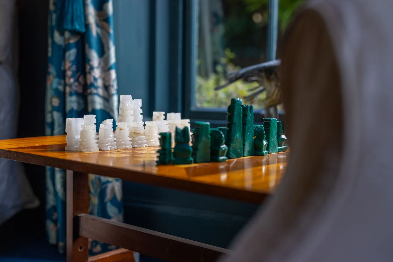 Chess set beside a window with patterned curtains and garden outlook