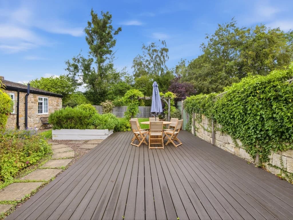 Spacious decked patio with outdoor dining surrounded by mature landscaped gardens