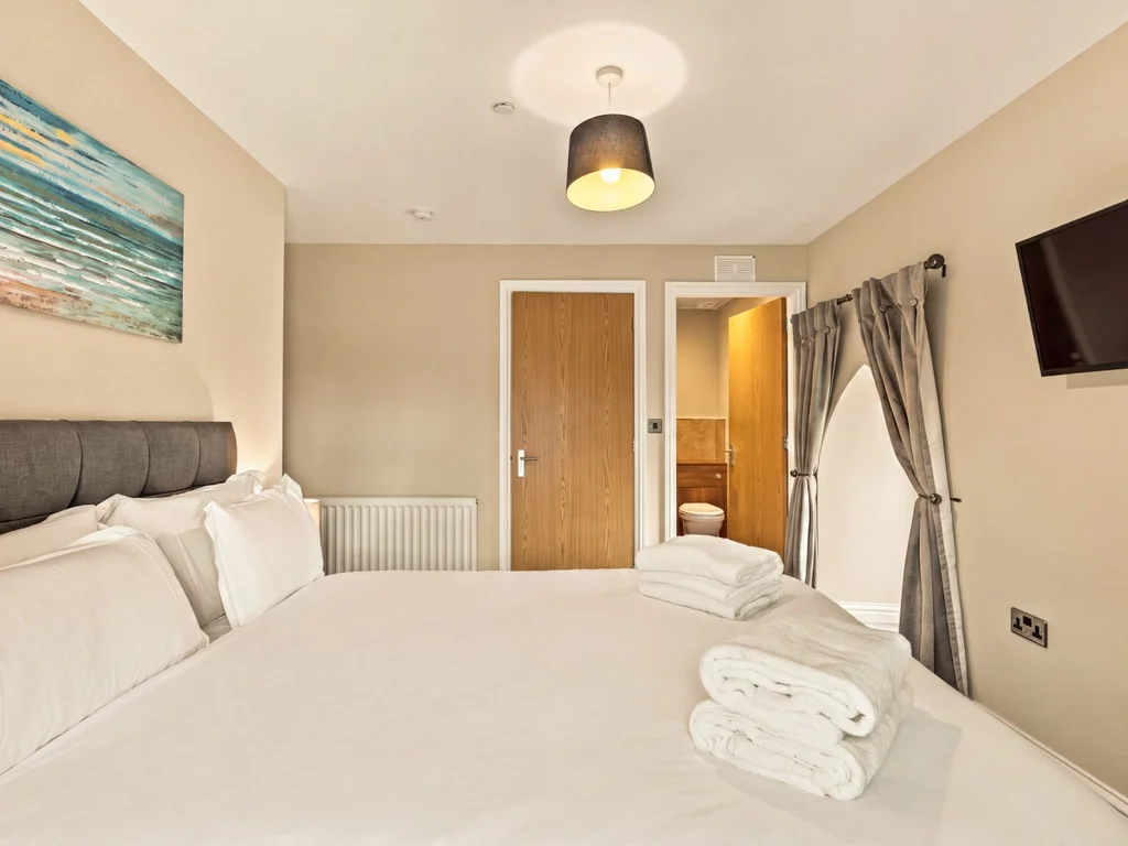 King bedroom with upholstered headboard, wall-mounted TV and en-suite.