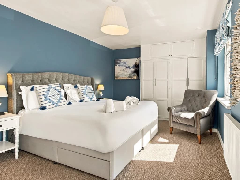 King bedroom with blue feature wall, fitted wardrobes and armchair.