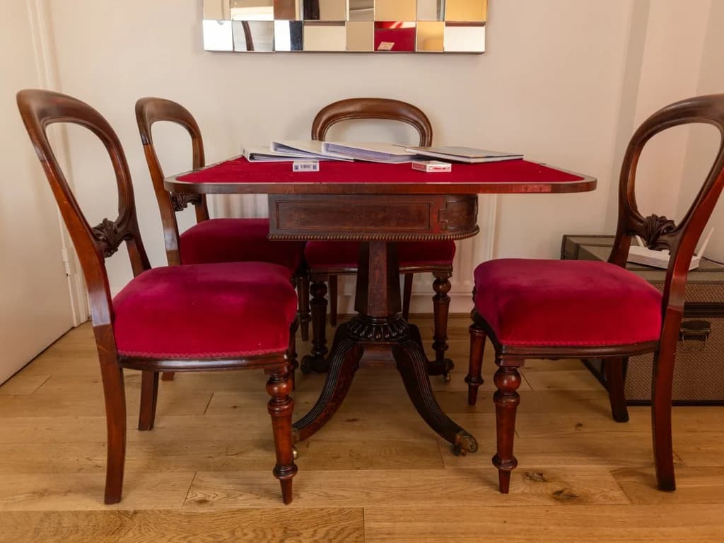 Antique card table with burgundy velvet chairs on hardwood flooring