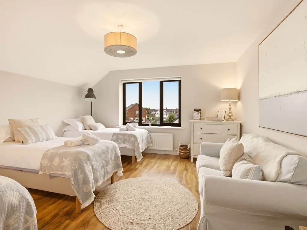 Family bedroom with three single beds, oak flooring and cosy sofa seating