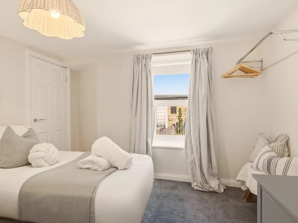 Twin bedroom with window, hanging rail and chest of drawers.