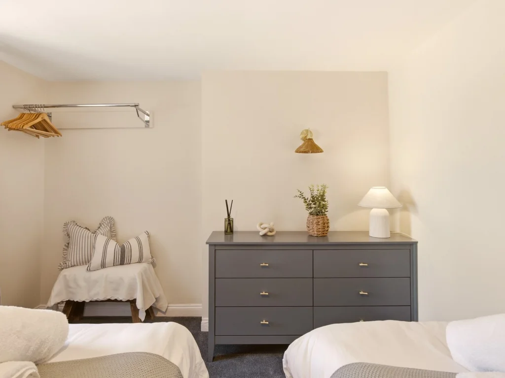 Twin bedroom with dresser, reading lamp and open hanging space.