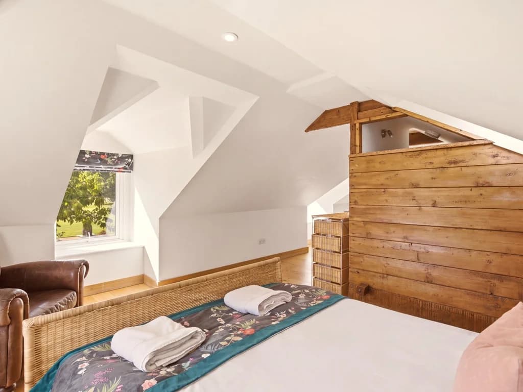 Hayloft bedroom framed by sloping ceilings and exposed timber beams
