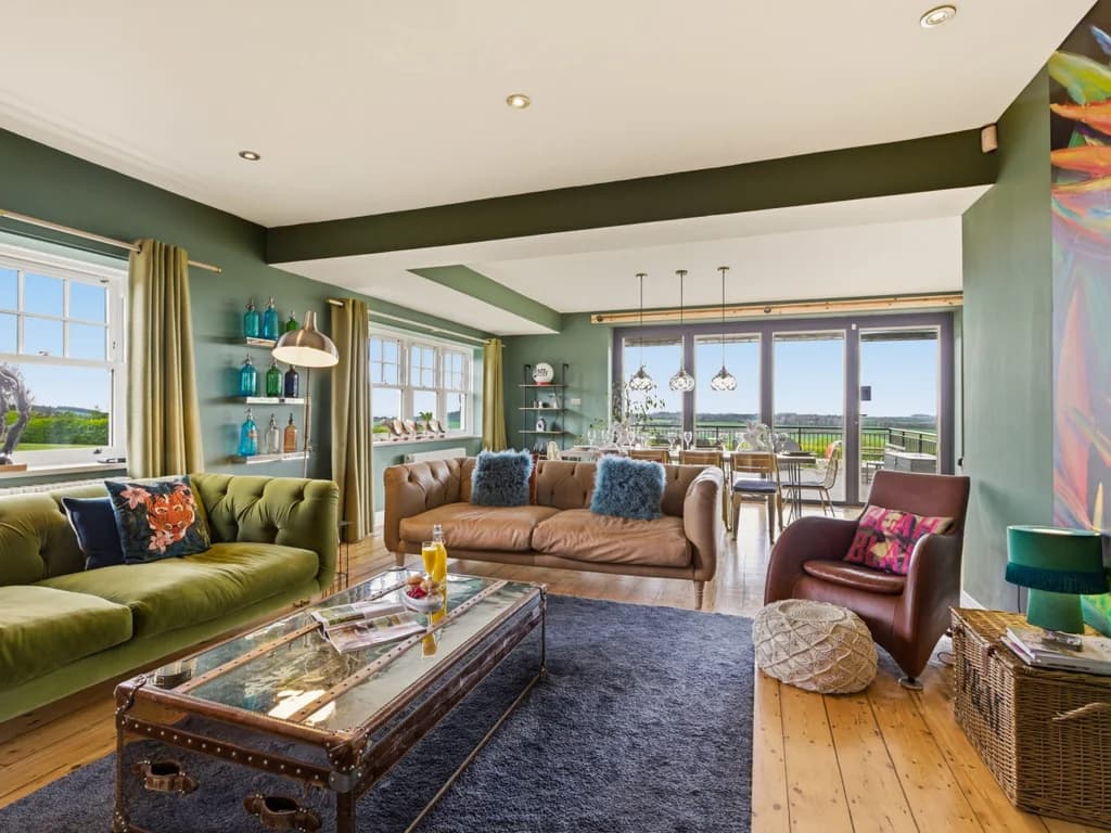 Open-plan lounge with a green velvet and leather sofa plus tropical mural.
