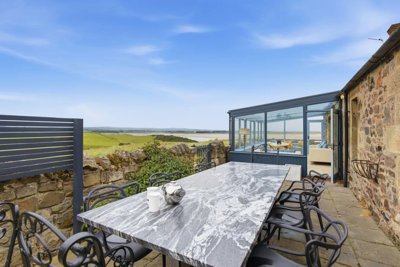 Marble outdoor dining table with Budle Bay view and glass conservatory