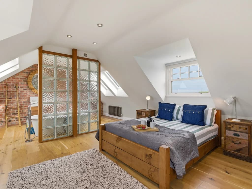 Bedroom 5 with king bed, exposed brick and freestanding bath behind glass.
