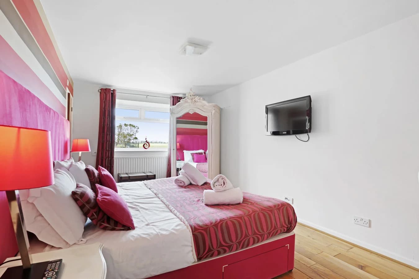King-size bedroom with pink upholstered headboard and TV