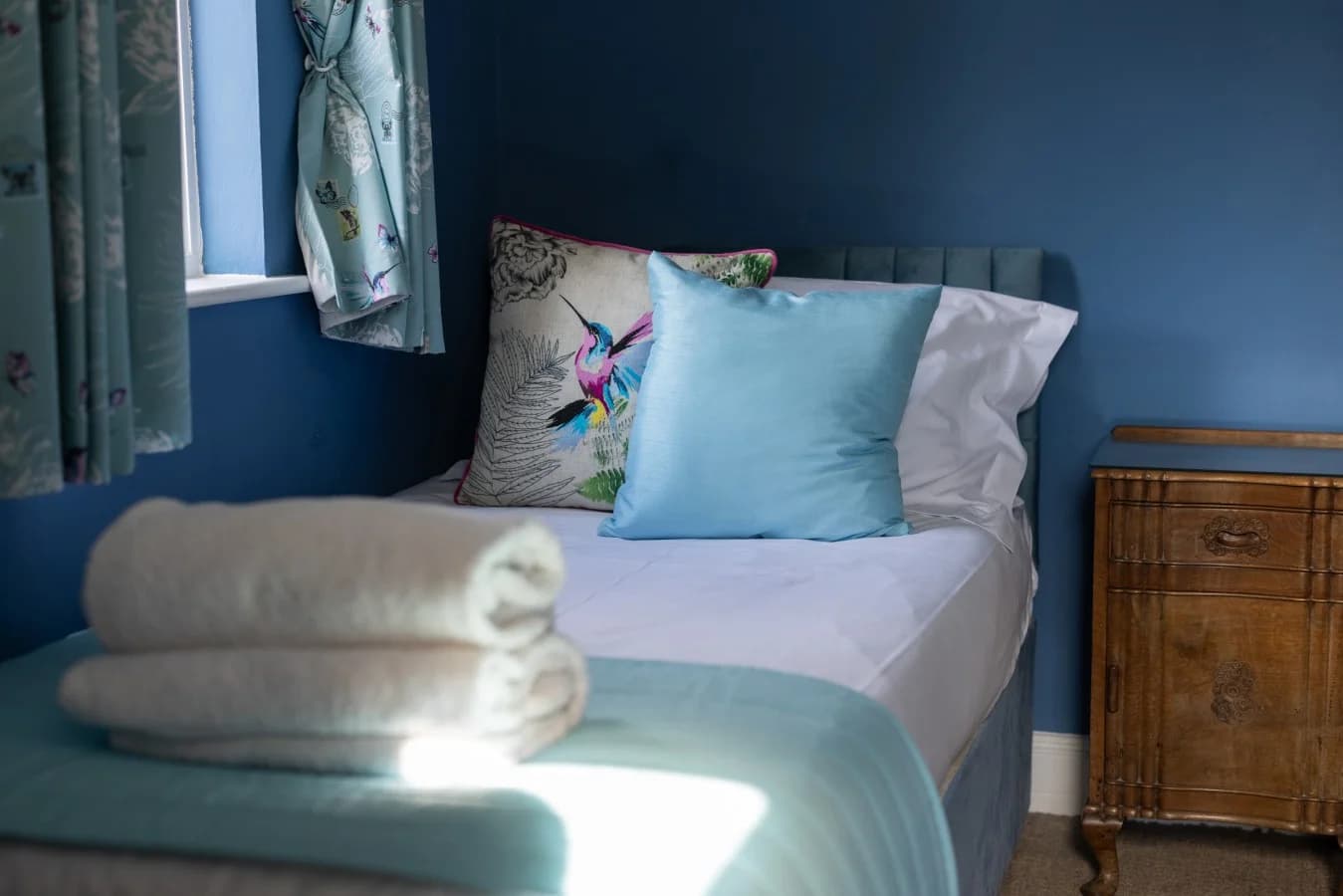 Twin bed with blue upholstered headboard and bird print cushions.