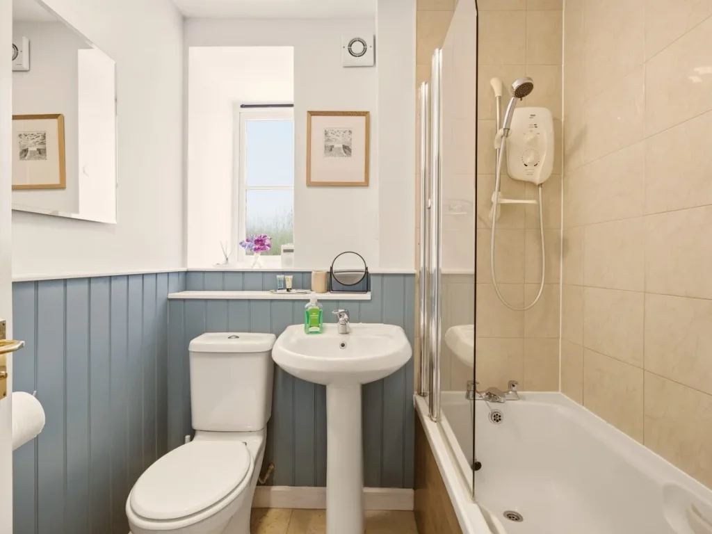 Family bathroom with bath, shower over, basin and blue wall panelling