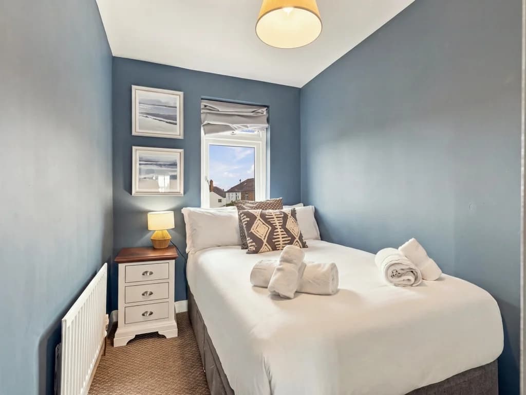 Small double bedroom with bedside table and coastal-inspired artwork.