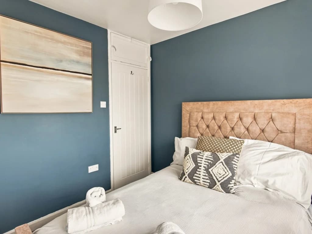 King bedroom with upholstered headboard and deep blue feature wall.