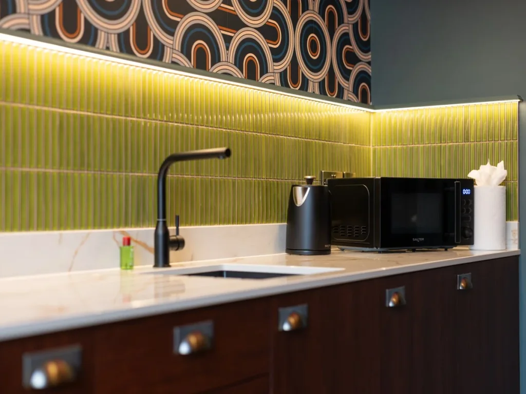 Kitchen sink and appliances beneath the illuminated tiled splashback.