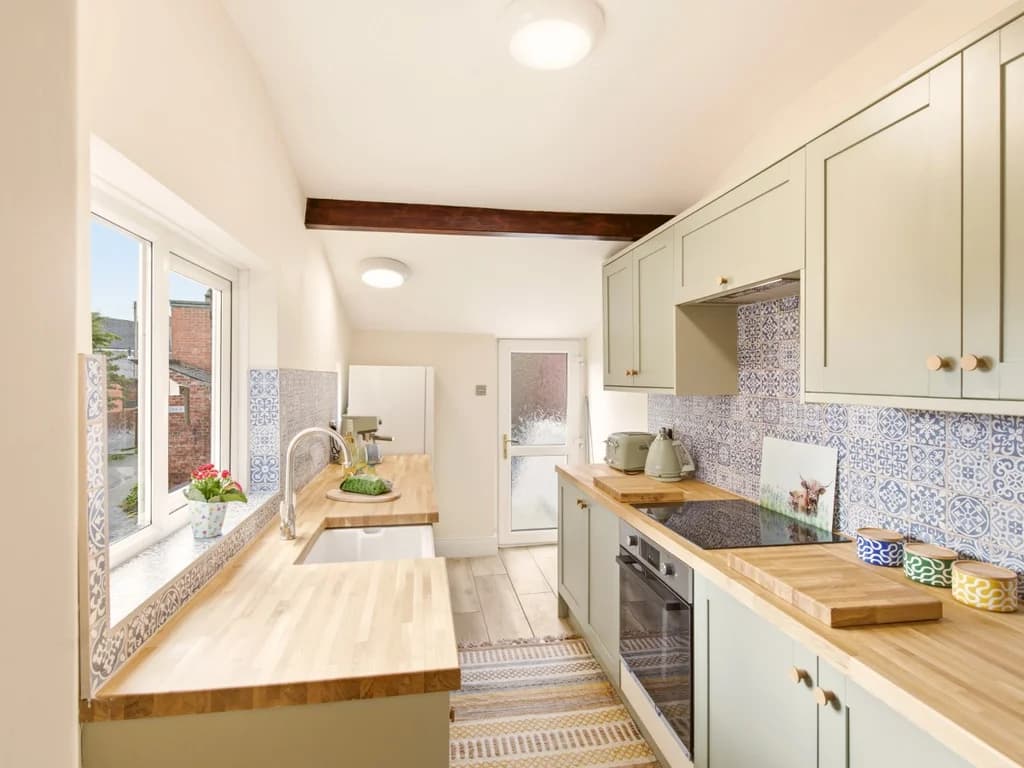 Galley kitchen with wooden worktops and blue patterned splashback.