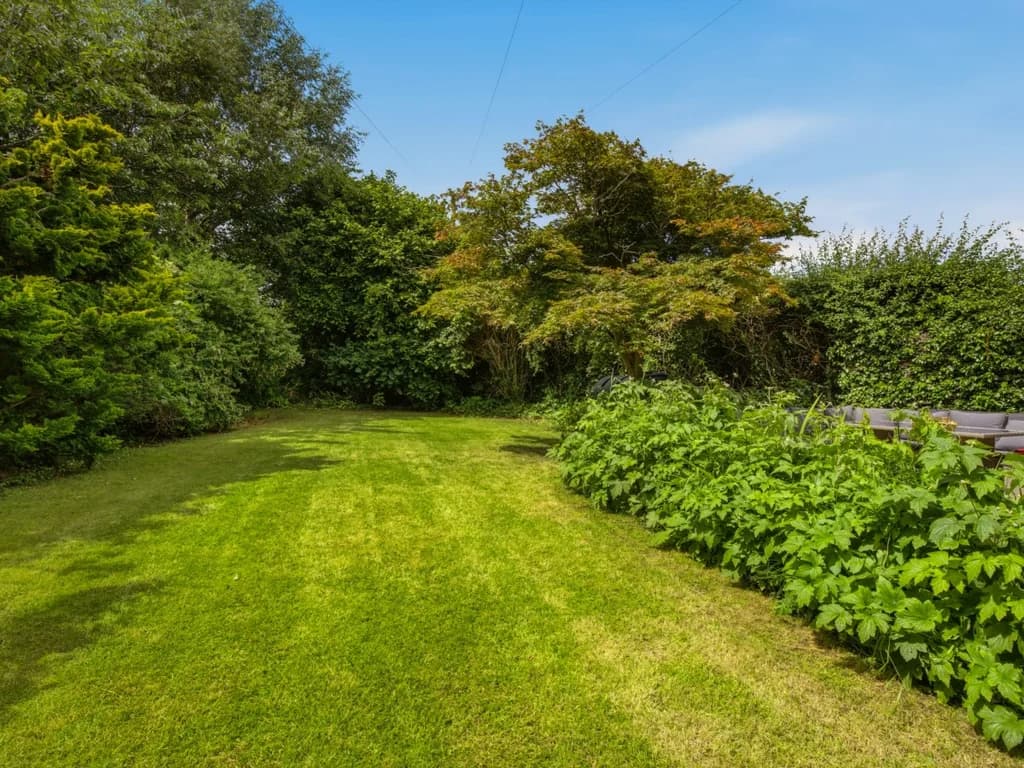 Spacious lawned garden bordered by mature trees and colourful cottage planting