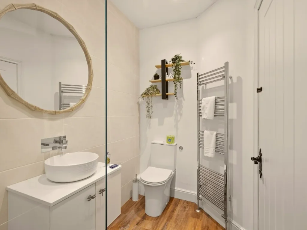 Modern ensuite with countertop basin, round mirror and heated towel rail.