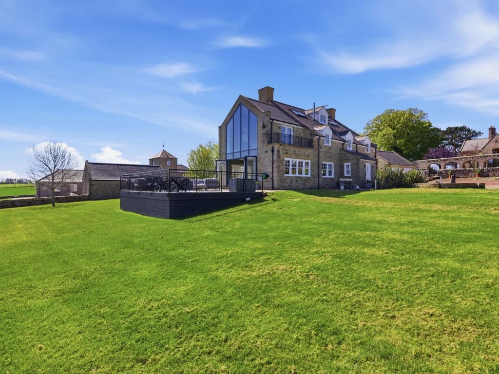 Stone farmhouse exterior with statement gable glazing and private lawn.