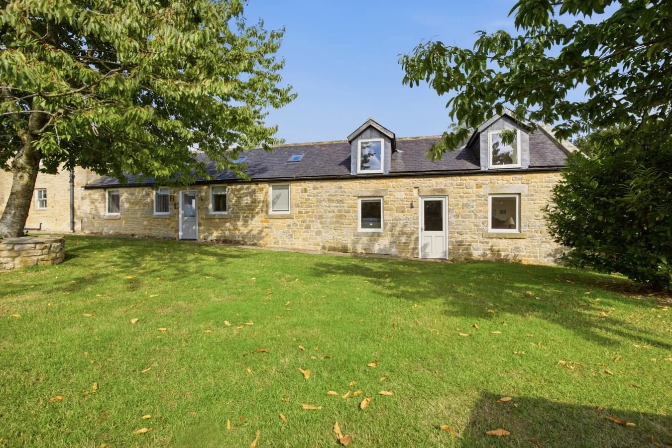 Stone cottage exterior overlooking the shared lawn and mature trees
