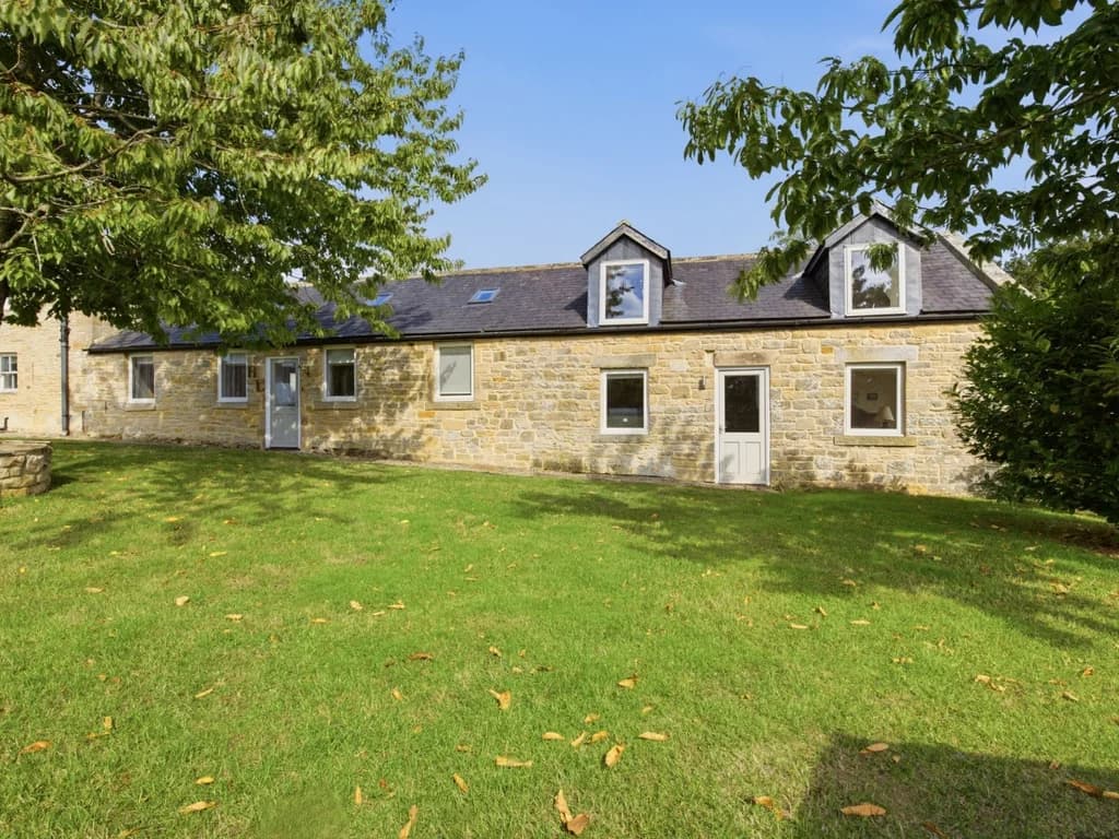 Stone cottage exterior overlooking the shared lawn and mature trees