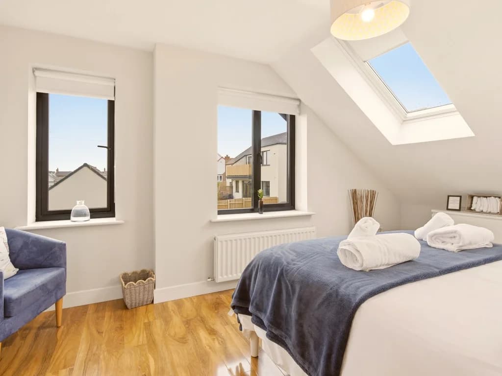 Bright first-floor king bedroom with skylights and soft blue armchair