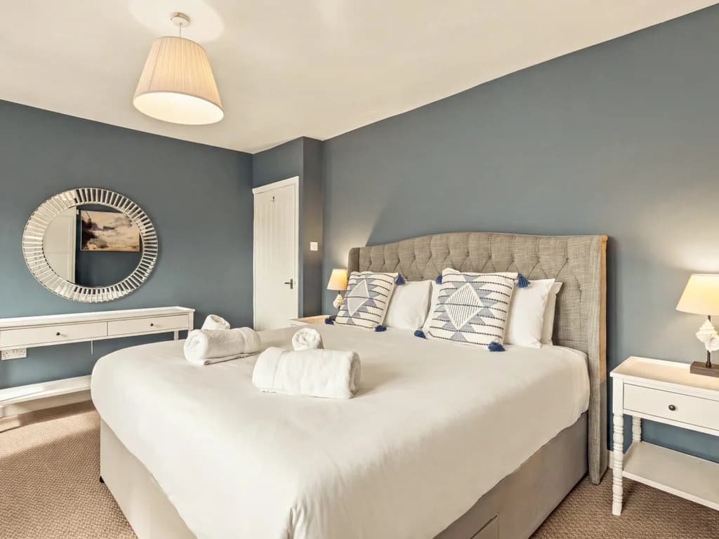 Spacious king bedroom with dressing table and round statement mirror.