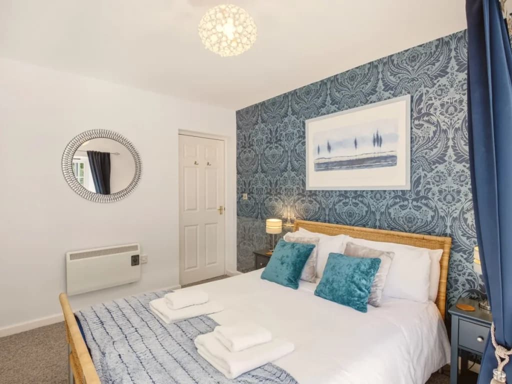 King bedroom with blue feature wall, woven bed frame and coastal artwork