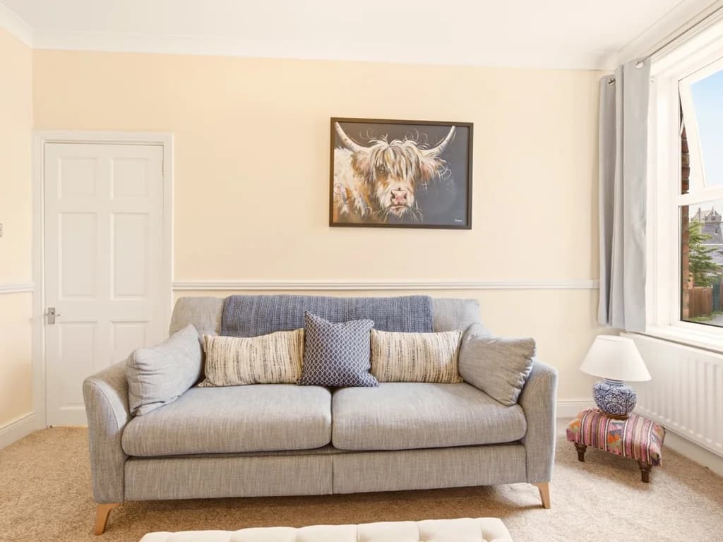 Grey sofa beneath Highland cow artwork in the living room.