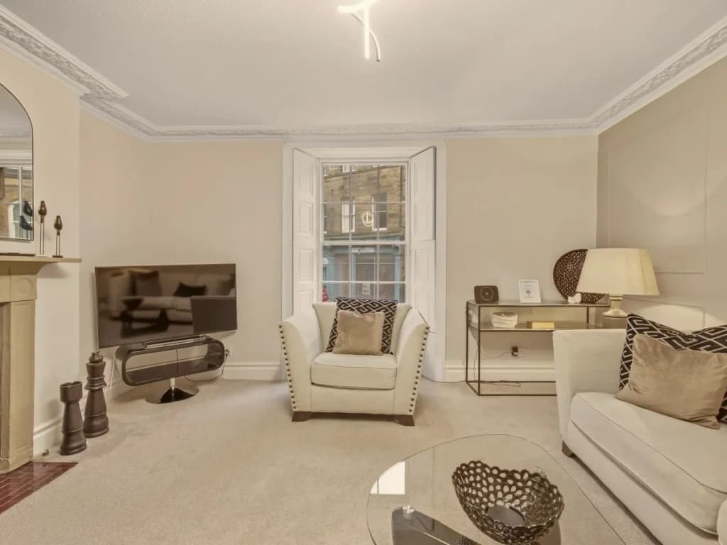 Bright living area with Smart TV, armchair and tall sash window.