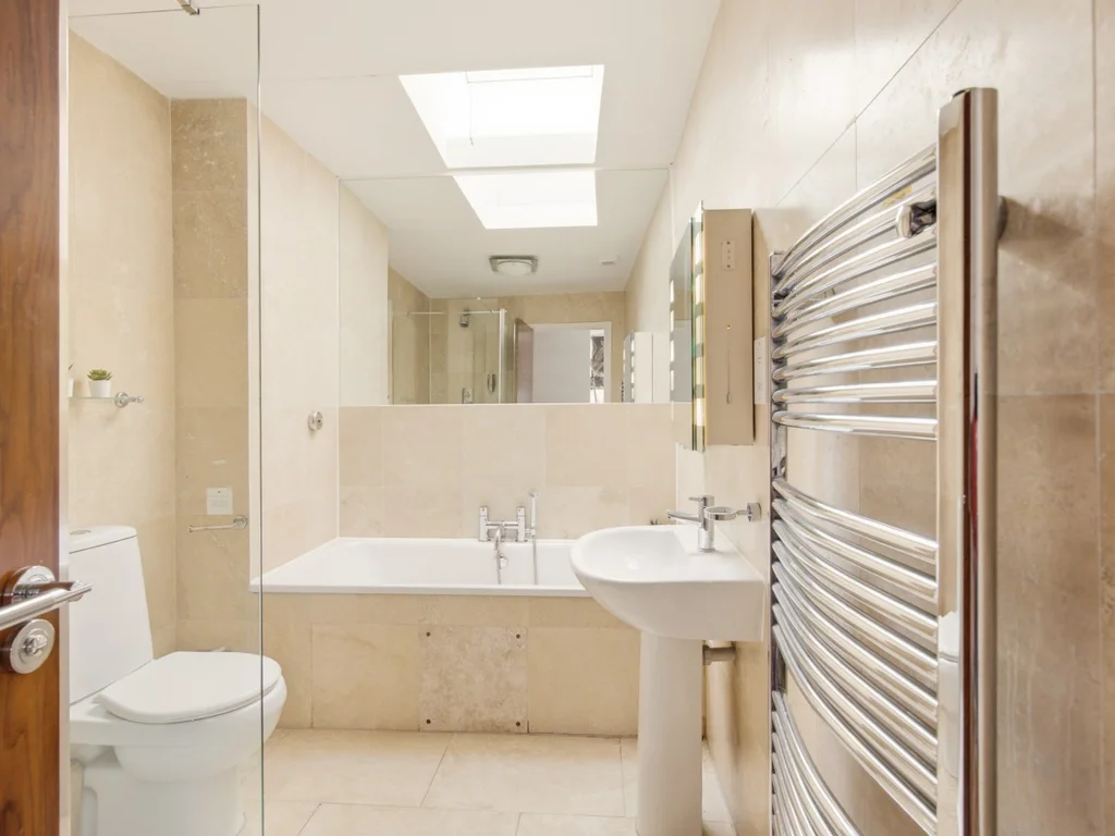 Beige tiled bathroom with bath, washbasin, toilet and heated rail.