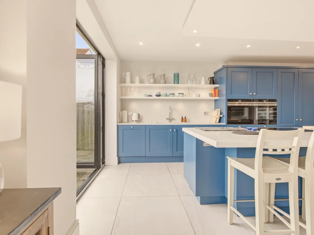 Breakfast bar with white stools, blue kitchen units and open display shelving