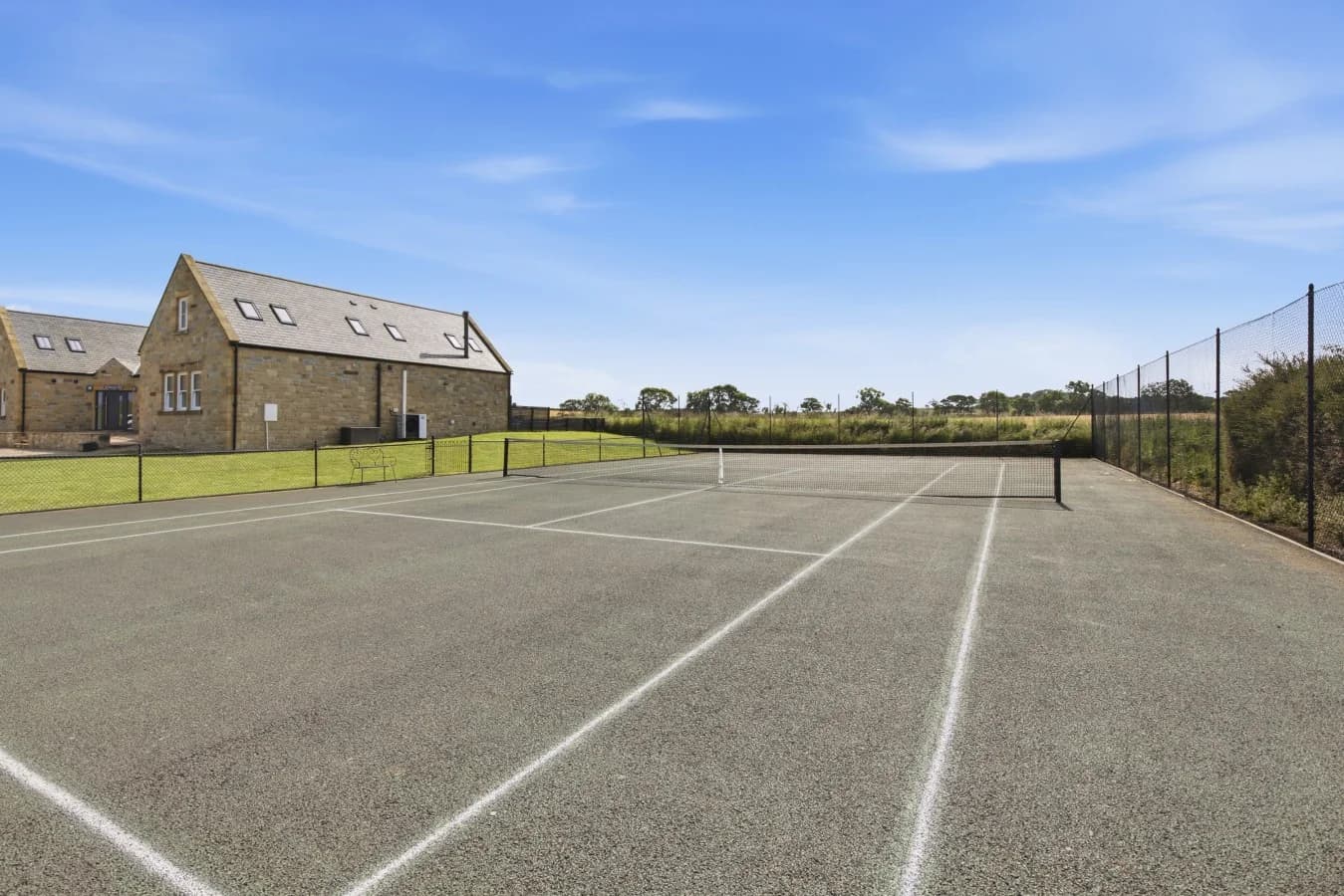 Fenced tennis court surrounded by open countryside