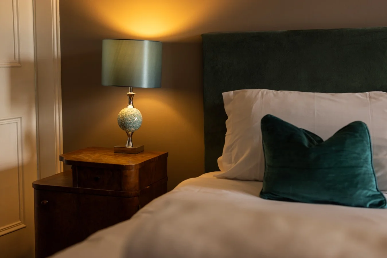 Walnut bedside table with teal lamp beside the super king bed.