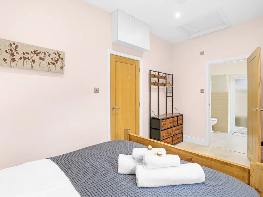 Soft pink walls and a warm wooden bed frame create an inviting atmosphere in this cosy bedroom, leading to a bathroom.