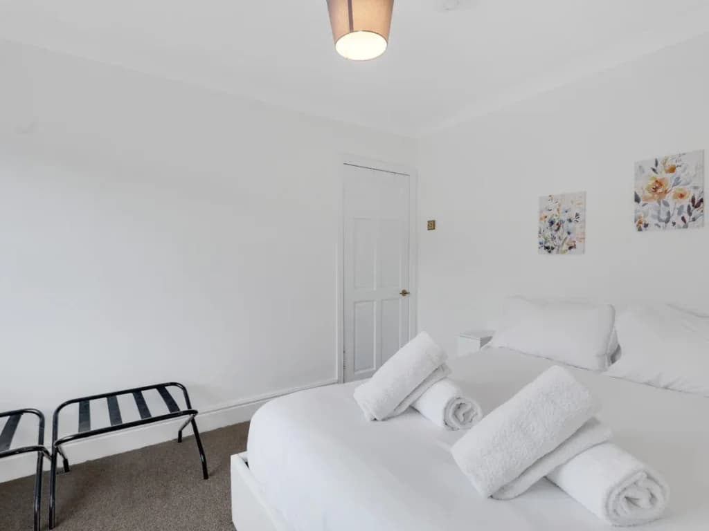 Bright king bedroom with fresh white bedding, towels and luggage racks