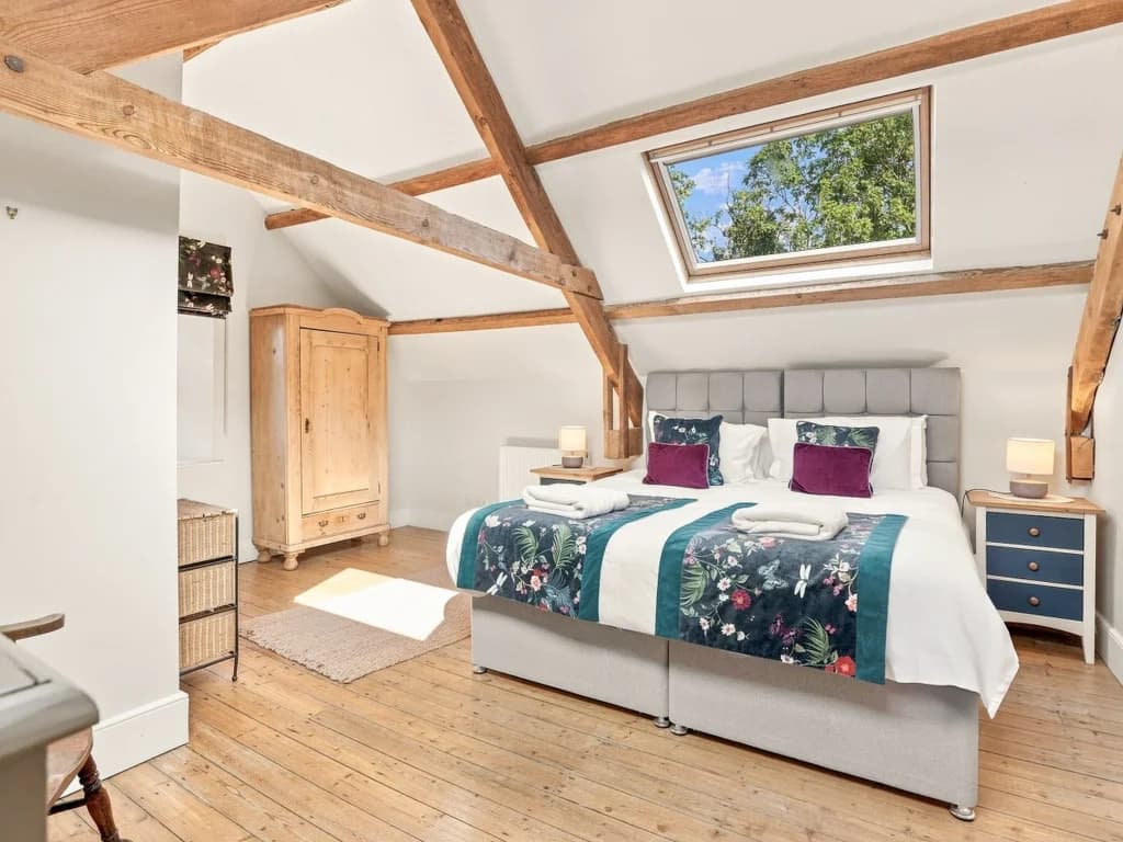 Spacious bedroom with skylight, exposed beams and wooden flooring