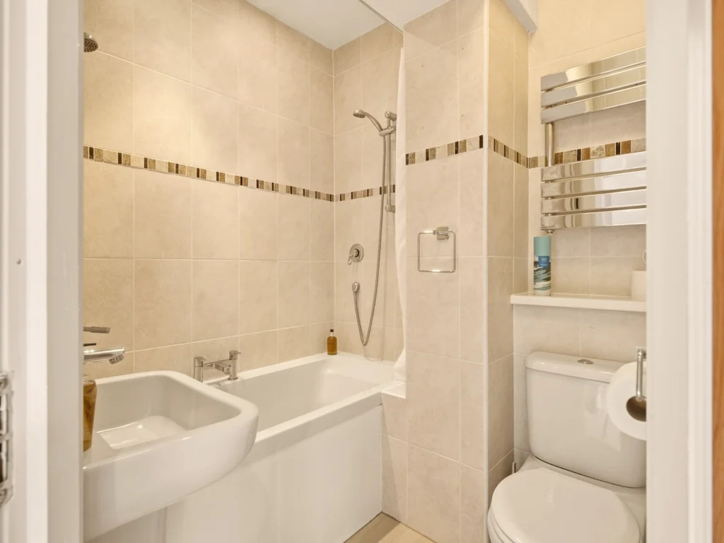 Modern en-suite bathroom featuring a bath with overhead shower and heated towel rail
