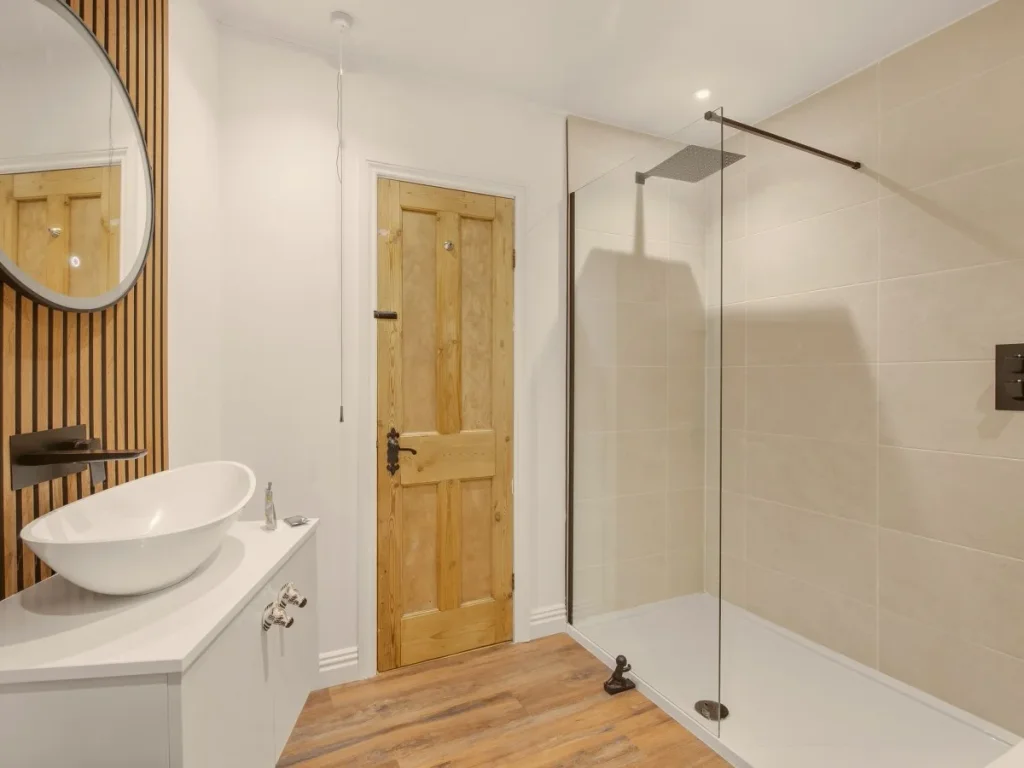 Spacious bathroom with rainfall shower, glass screen and wood flooring.