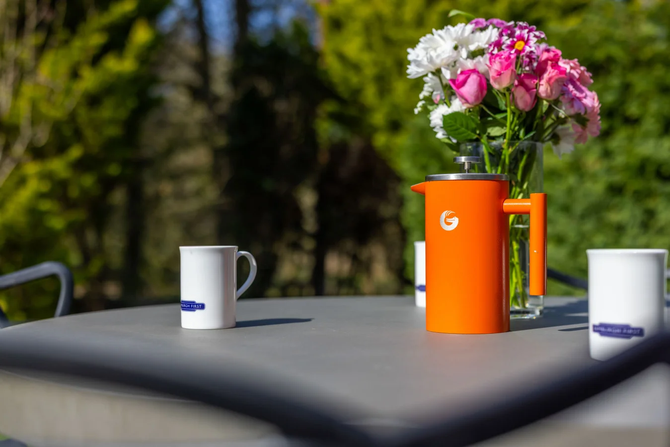 Outdoor dining table with floral centrepiece and Bamburgh First mugs