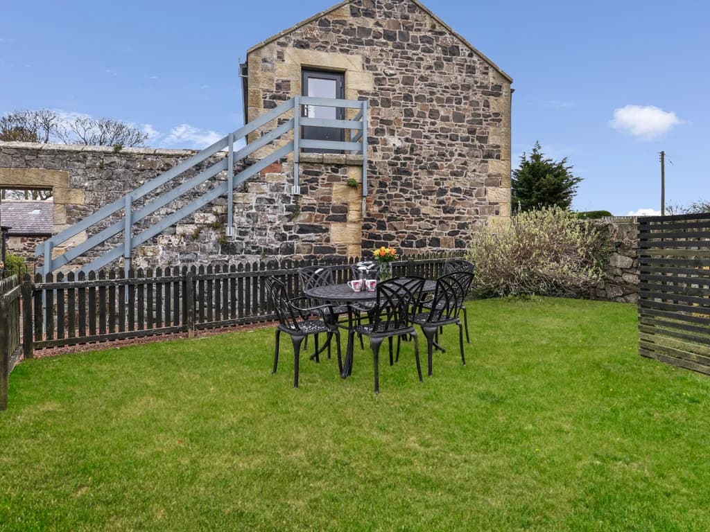 Enclosed lawned garden with outdoor dining area and sandstone exterior